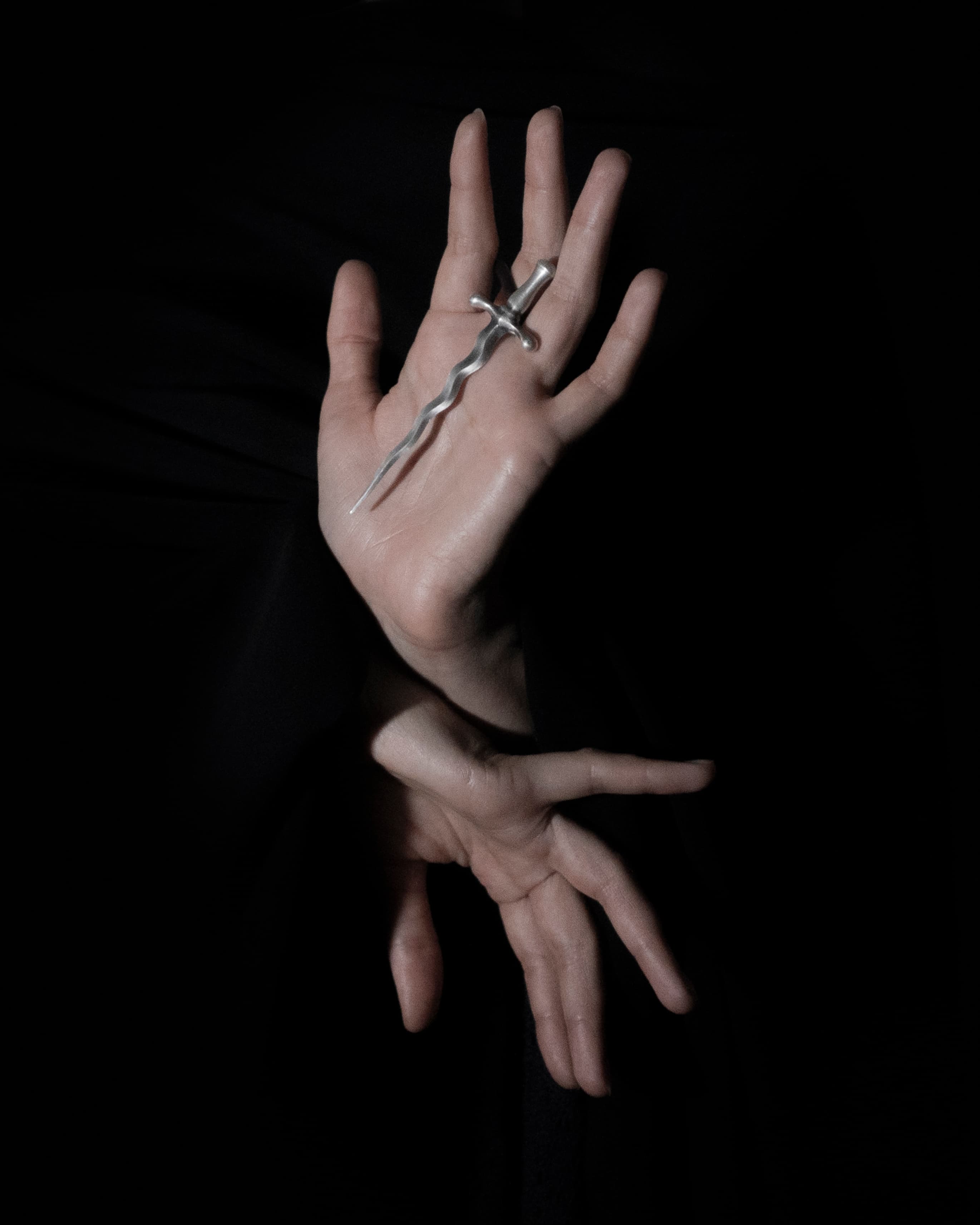 A silver-toned wavy dagger pendant resting across an open hand against a dark background