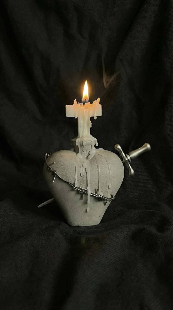 Stone Sacred Heart sculpture wrapped in barbed wire, pierced by a miniature sword, topped by a burning cross-shaped candle